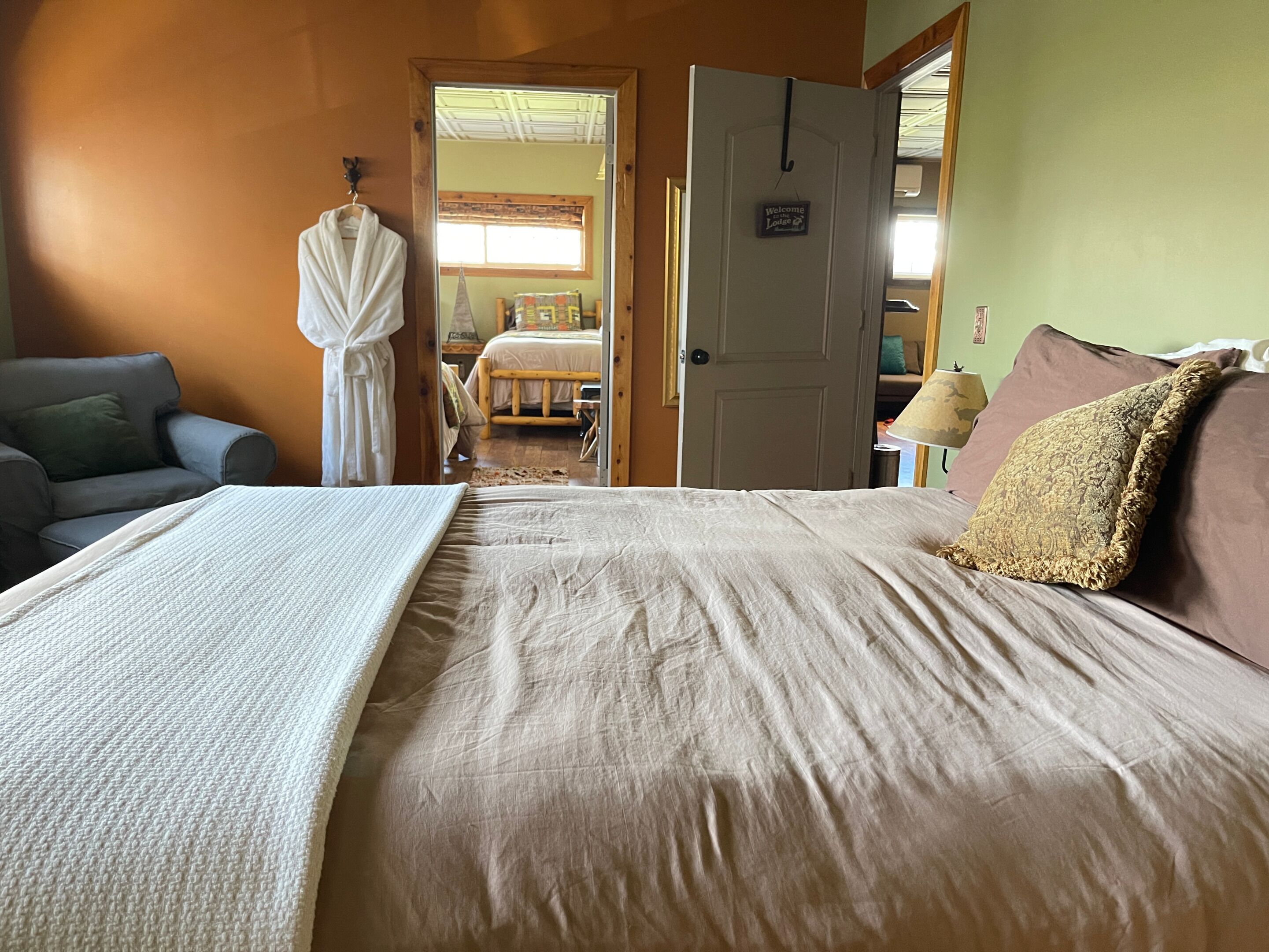 Un dormitorio con cama, una silla, una bata y una puerta que da a otra habitación.