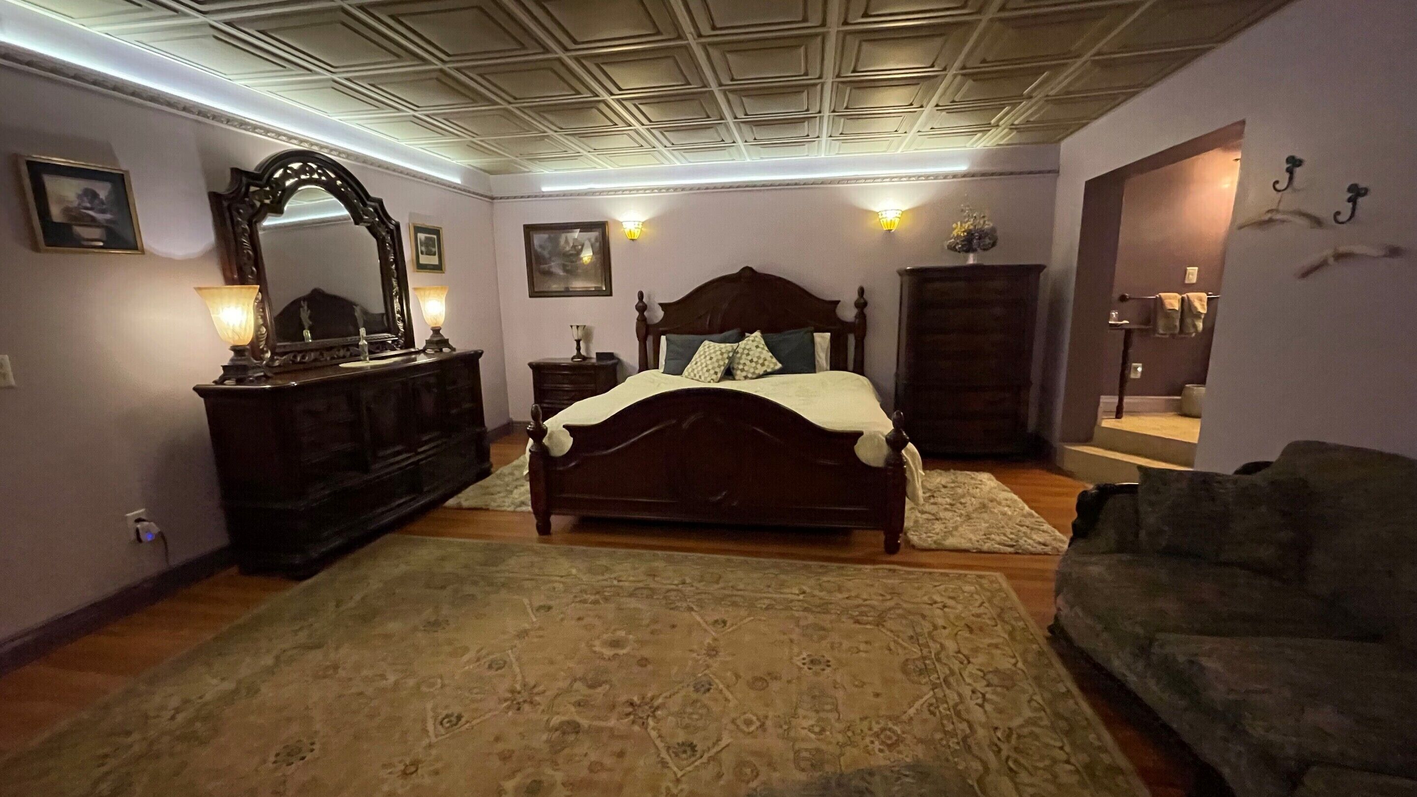 Een slaapkamer met een groot bed, een dressoir, een spiegel en een bank.