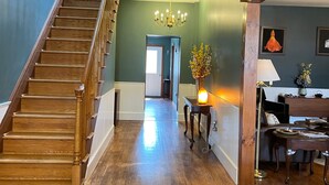 A wooden staircase leading to a second floor, a chandelier, a dining area with a table and chairs, and a vase with flowers on a side table. - The Yorkshire Inn (Phelps)