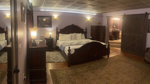 A bedroom with a large bed, a dresser, a nightstand, a mirror, and a door leading to a bathroom. - The Yorkshire Inn (Phelps)