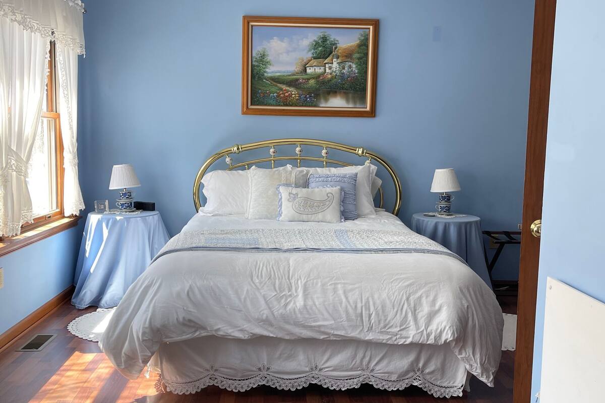 A bedroom with a bed, two bedside tables, a chandelier, a painting, and a patterned rug.