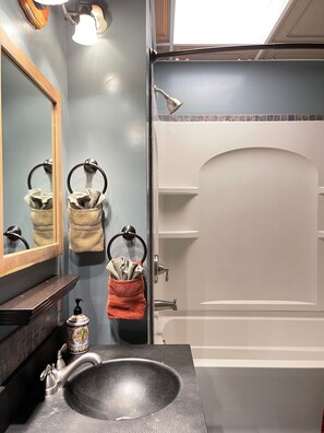 A bathroom with a dark sink, a mirror, and two towel rings with towels.