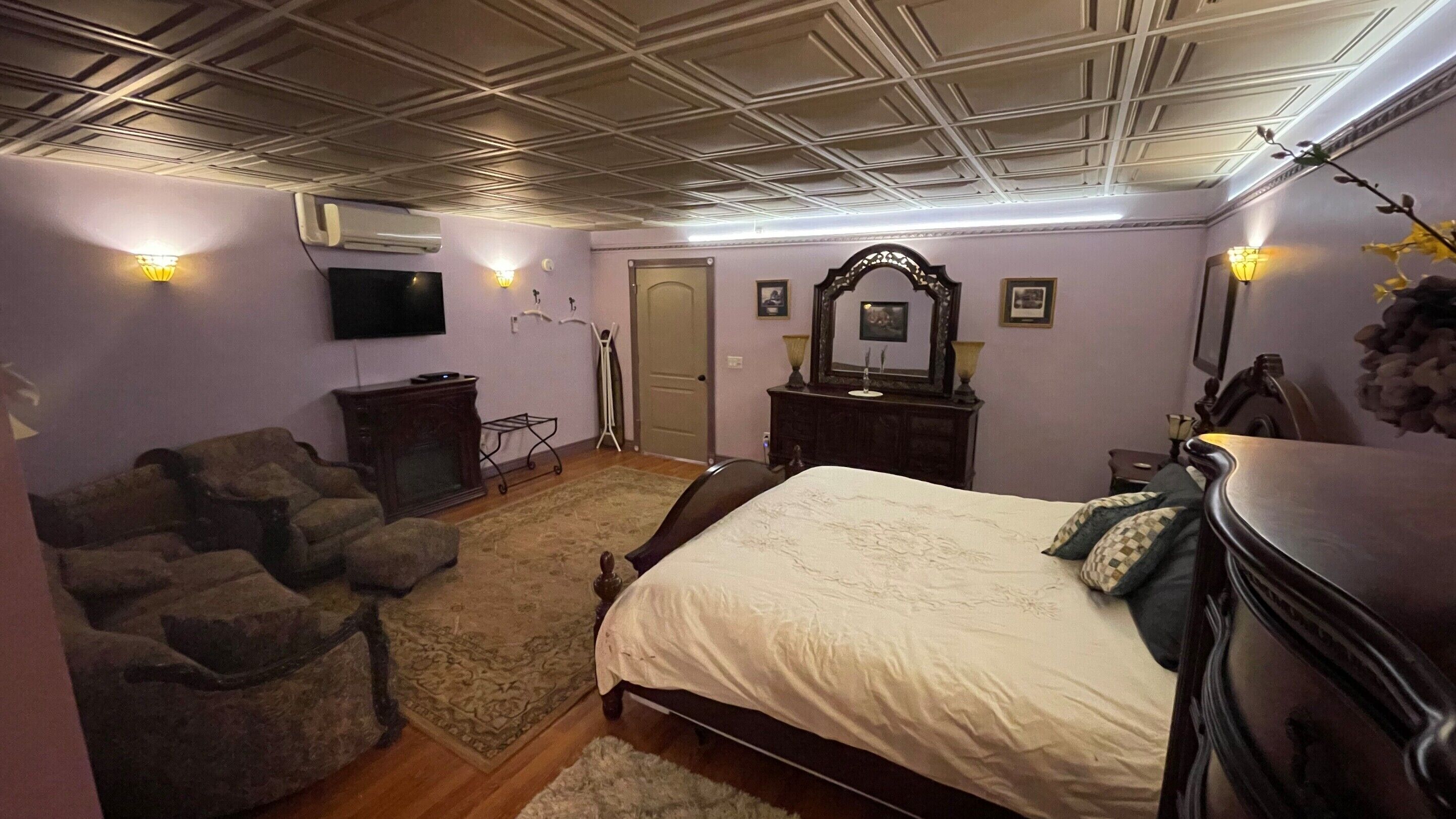 A bedroom with a bed, a dresser, a TV, a mirror, and a door.