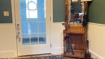 A room with a wooden floor, a floral patterned rug, a white door with frosted glass panels, and a wooden mirror with a dog sign.