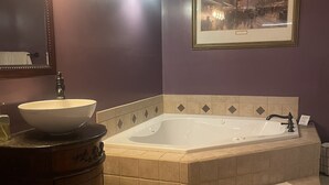 A bathroom with a large bathtub, a sink with a bowl, a vanity, and a framed picture on the wall. - The Yorkshire Inn (Phelps)