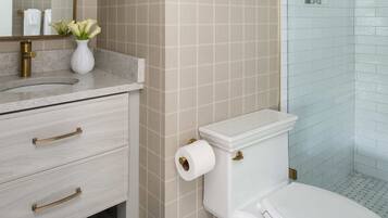 A bathroom with a toilet, a sink with a vase of flowers, and a shower area.