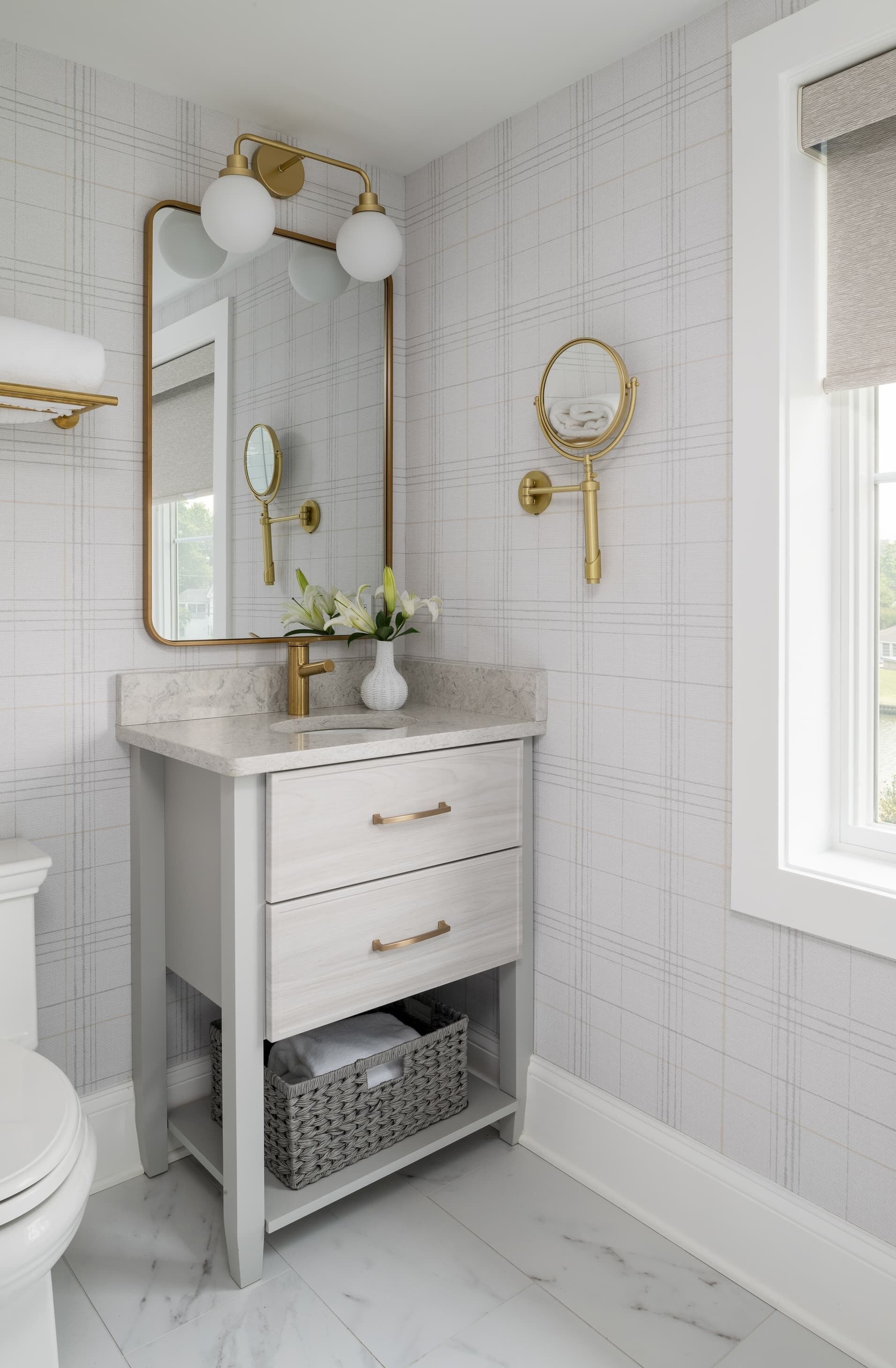 Une salle de bain avec un meuble-lavabo blanc, des robinetteries dorées, un miroir et une fenêtre donnant sur un beau paysage.