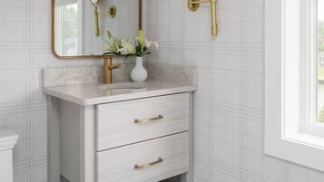 Une salle de bain avec un meuble-lavabo blanc, des robinetteries dorées, un miroir et une fenêtre donnant sur un beau paysage.