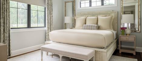 A bedroom with a large bed, bedside tables, a bench, and a window with curtains.