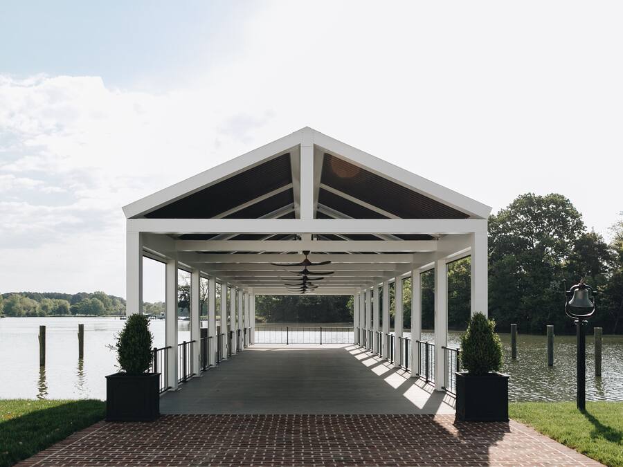 En överbyggd paviljong med ett tegelgolv, vita räcken och utsikt över en sjö.