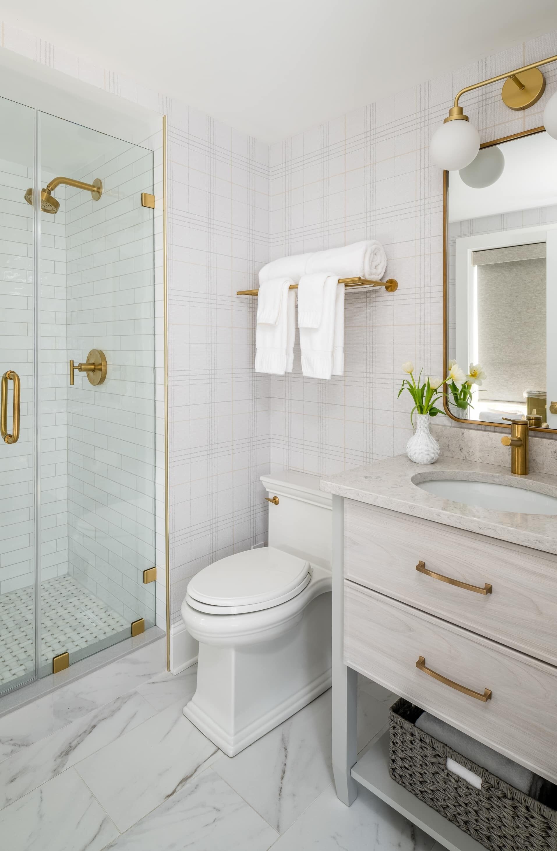 A modern bathroom with a glass-enclosed shower, a white toilet, and a vanity with a mirror and a vase of flowers.