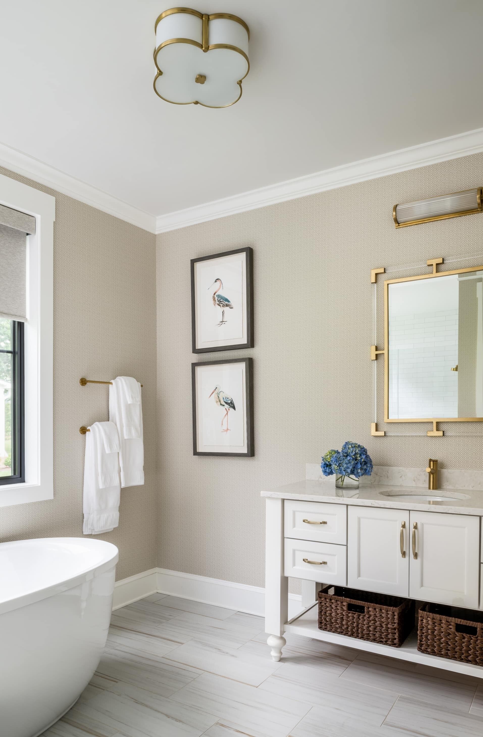 A bathroom with a white bathtub, a white vanity with gold handles, framed wall art, and a large mirror.
