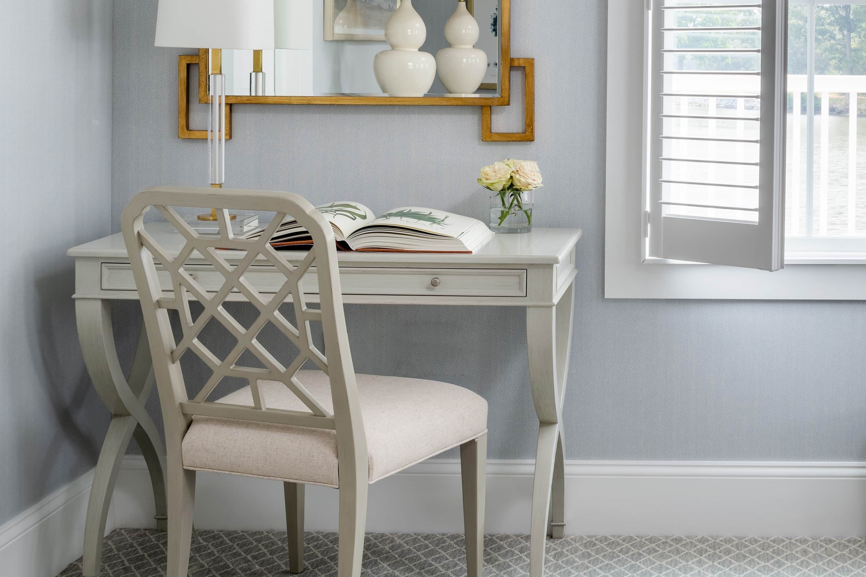 A white desk with a chair, a lamp, and a vase with flowers.