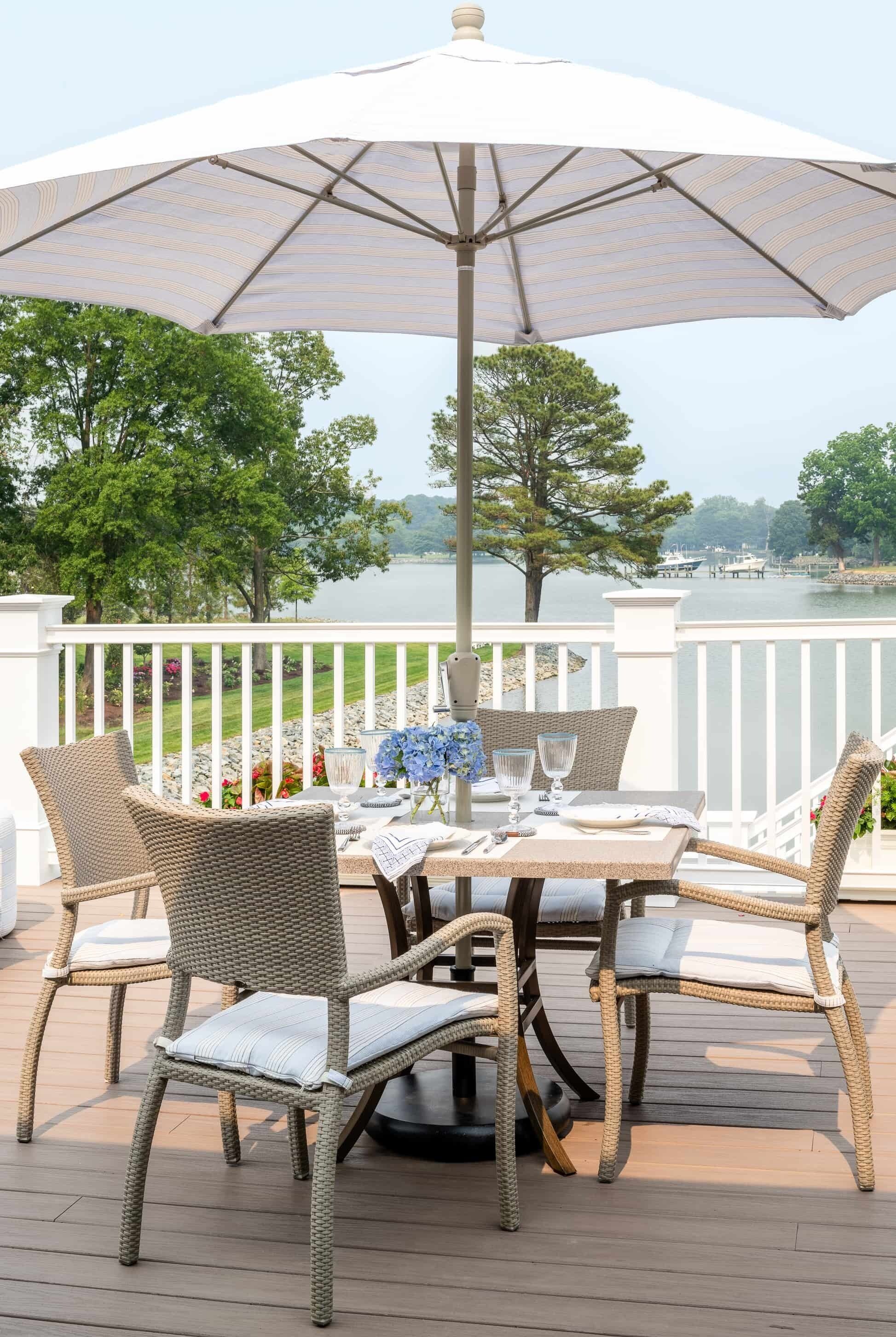 A deck with wicker chairs and a table set for dining, overlooking a lake.