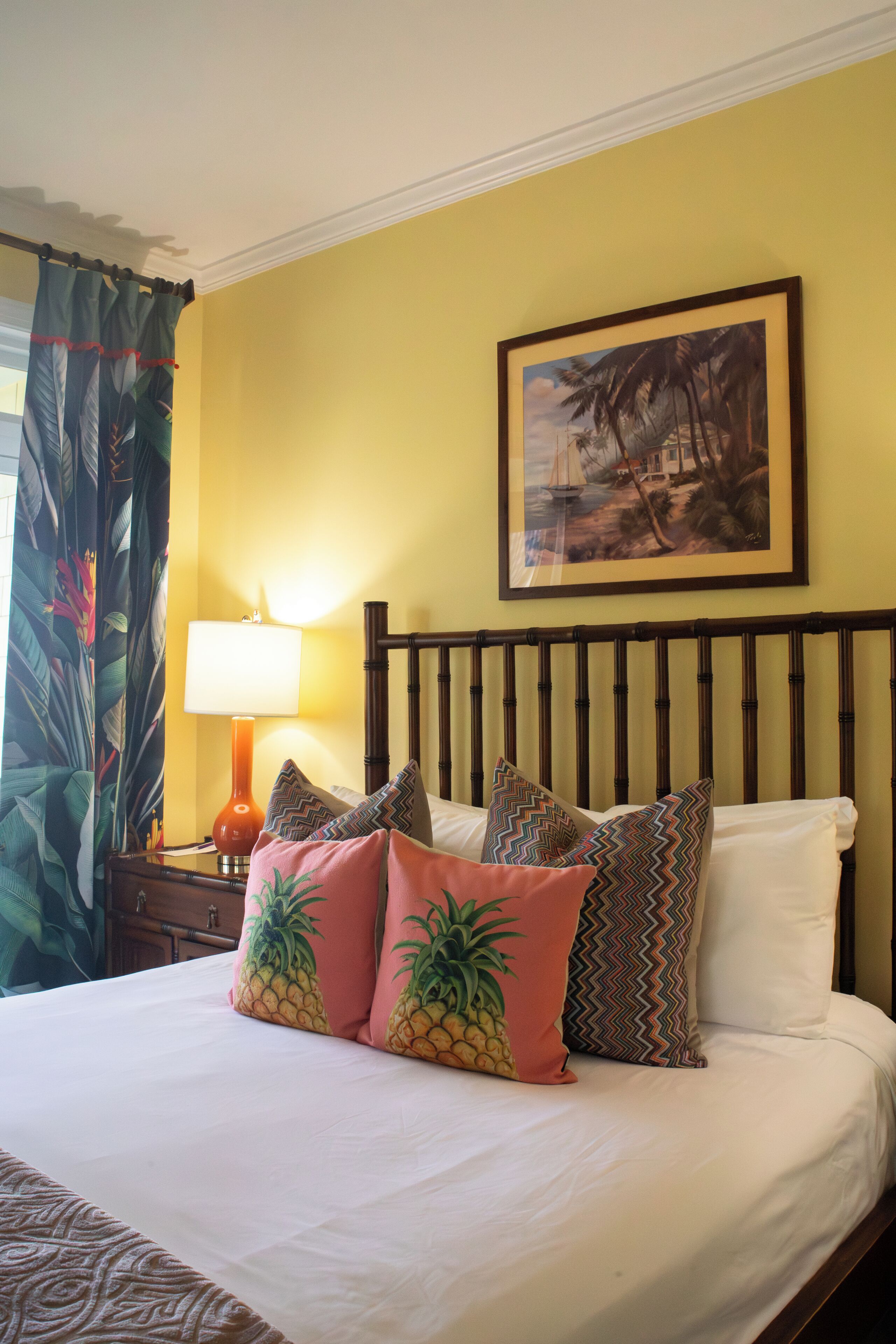 Una habitación de hotel con cama, mesita de noche, lámpara, un cuadro en la pared y cortinas.
