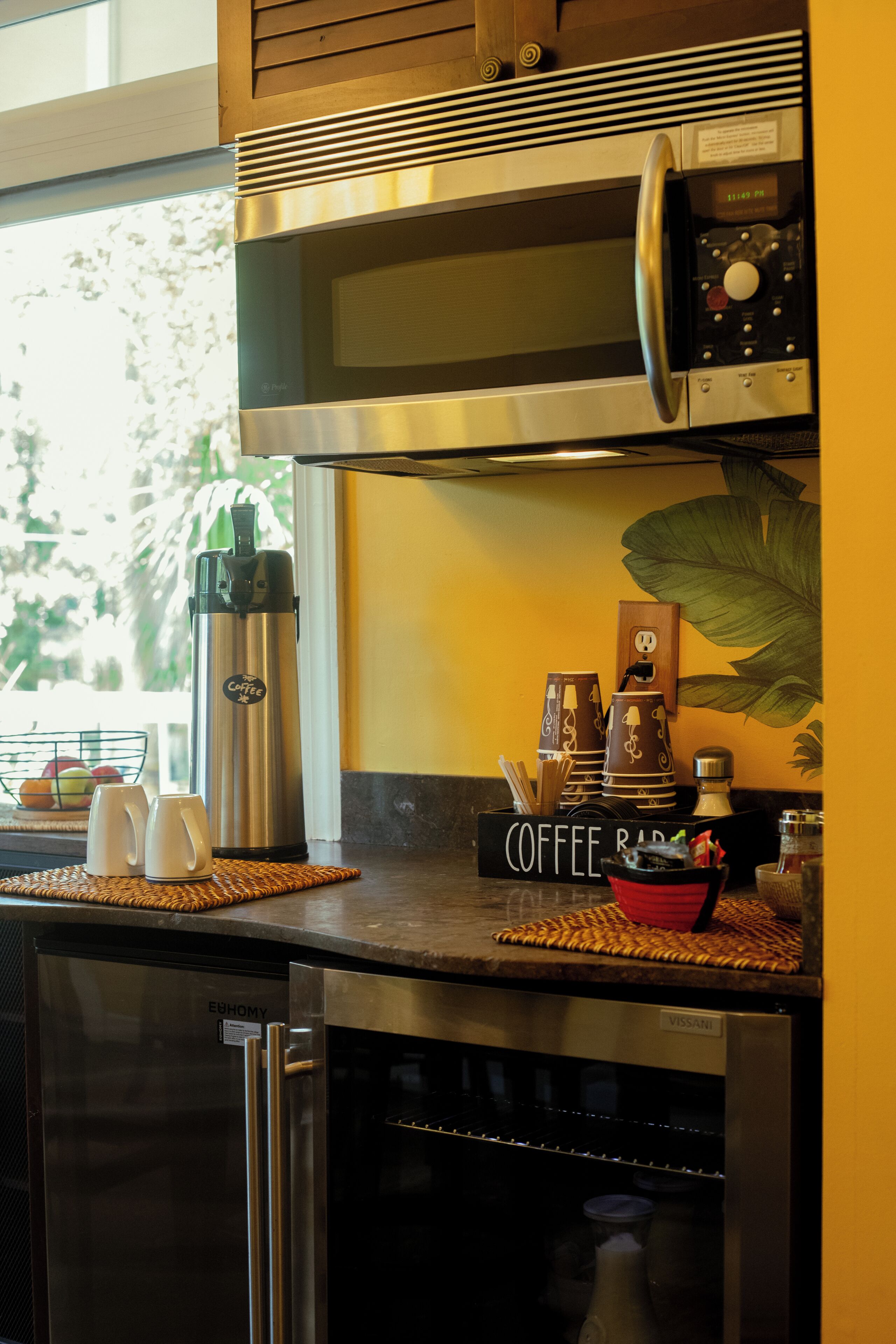 A kitchen with a coffee station, including a coffee maker, cups, and a sign that reads 'COFFEE BAR'.