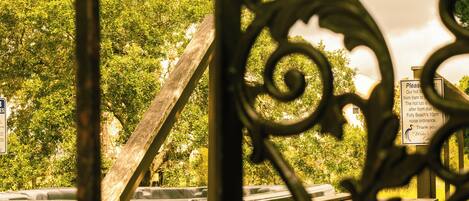 A wrought iron gate with a wooden structure behind it, a sign with text, and a view of trees.