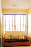 Una habitación con sofá, ventana con persianas y un respiradero en la pared.