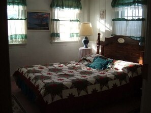 A bedroom with a bed, a nightstand, a lamp, and a window with curtains. - 1768 Country Inn (North Conway)