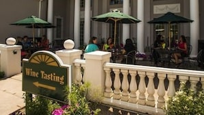 An outdoor seating area with tables and chairs, a sign for Wine Tasting, and a building with columns and arched windows. - Claremont Inn & Winery (Stratton)