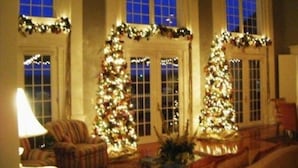 A warmly lit room with two Christmas trees, a lamp, and a sofa. - Claremont Inn & Winery (Stratton)