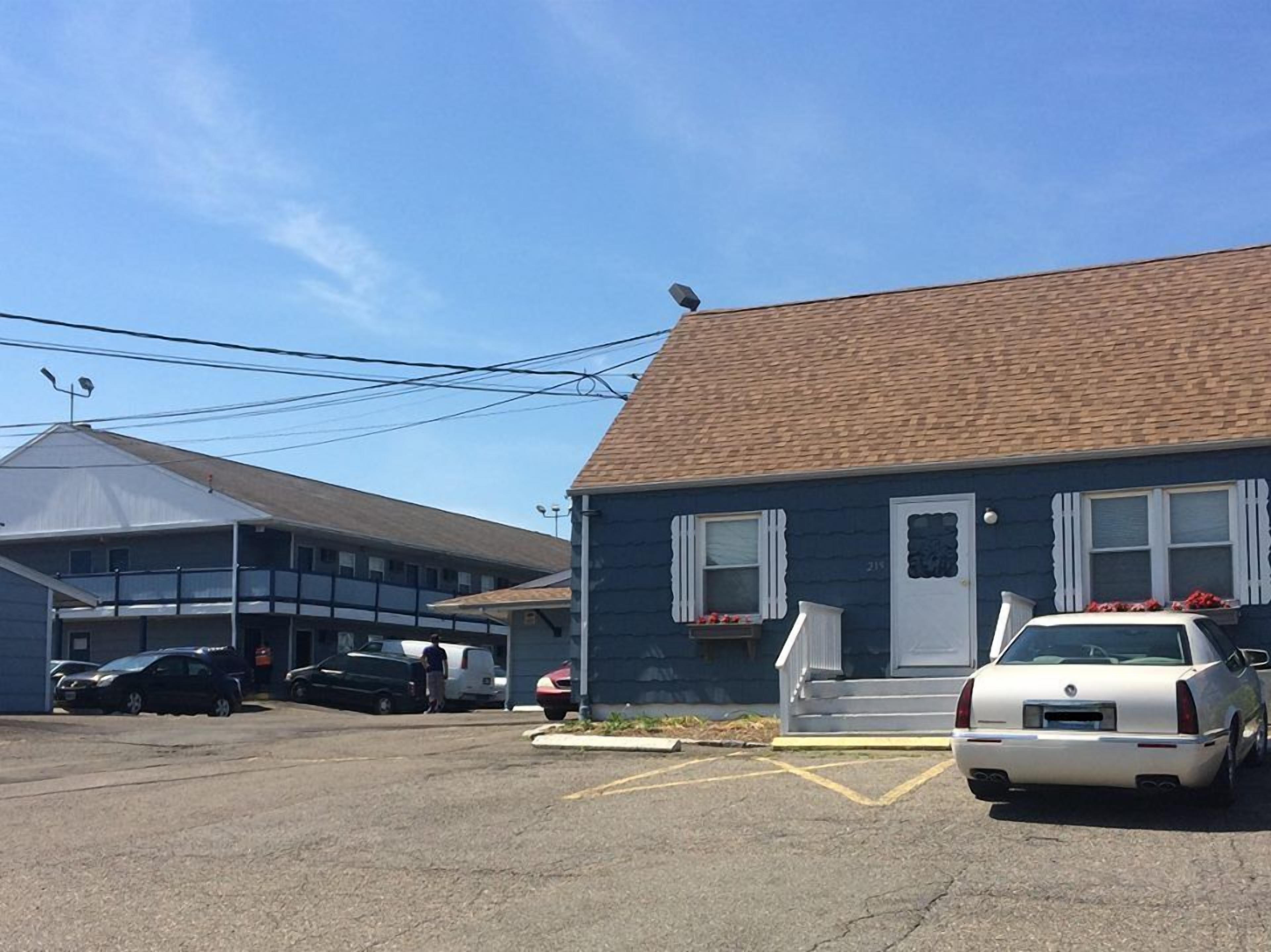 A building with a blue exterior and a brown roof, a white car parked in front, and a parking lot with several other cars.