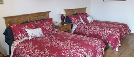 A room with two beds, each with red bedding and white tree patterns, a wooden headboard, a nightstand with a lamp, and a framed picture on the wall.