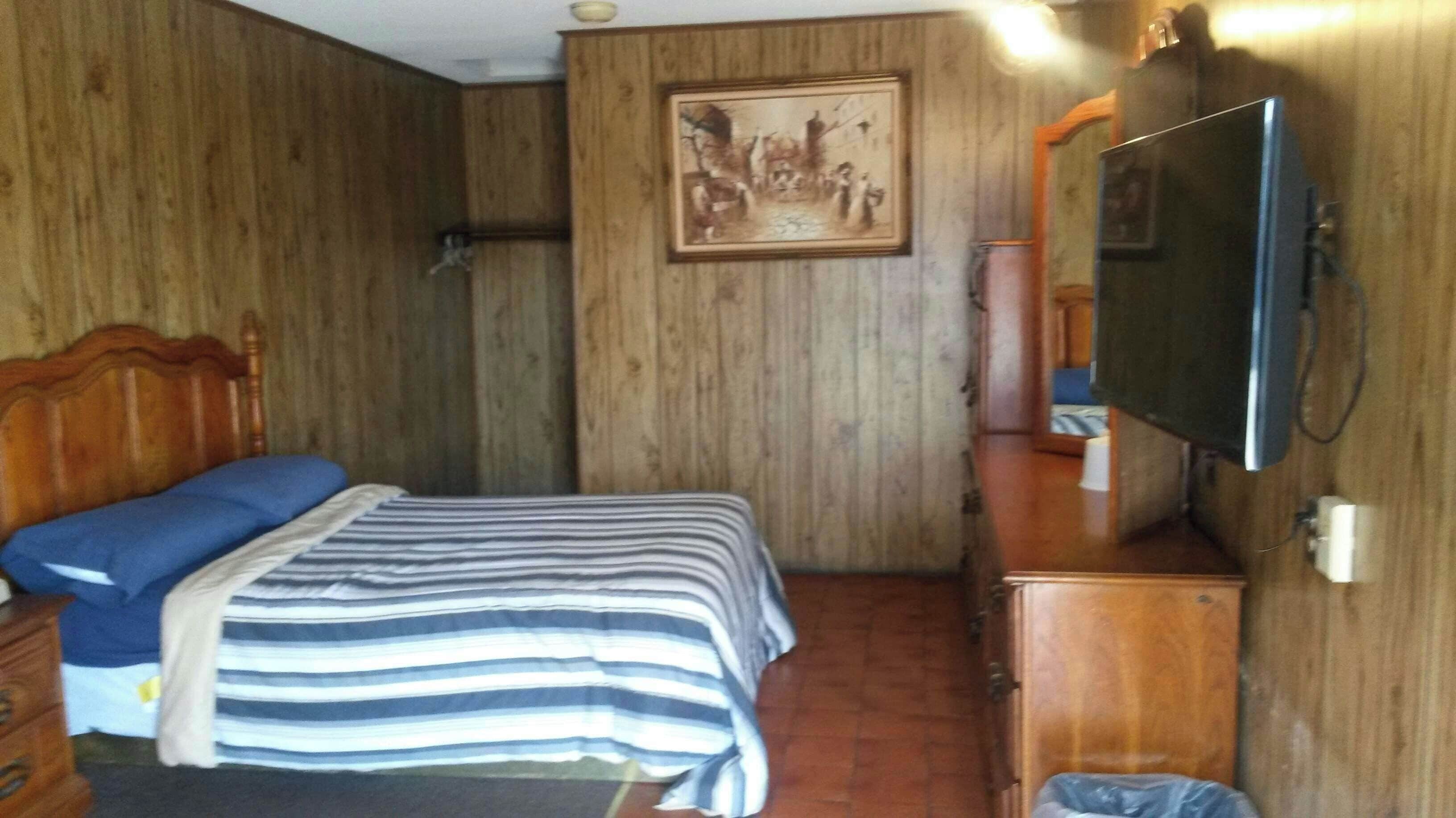 Quarto com cama, cabeceira de madeira, televisão e um quadro na parede.