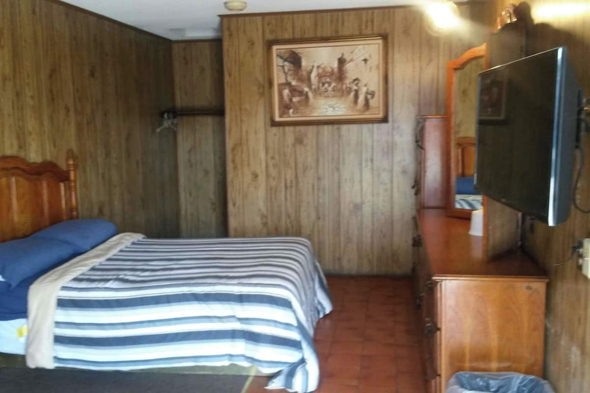 A room with a bed, a wooden headboard, a television, and a painting on the wall.
