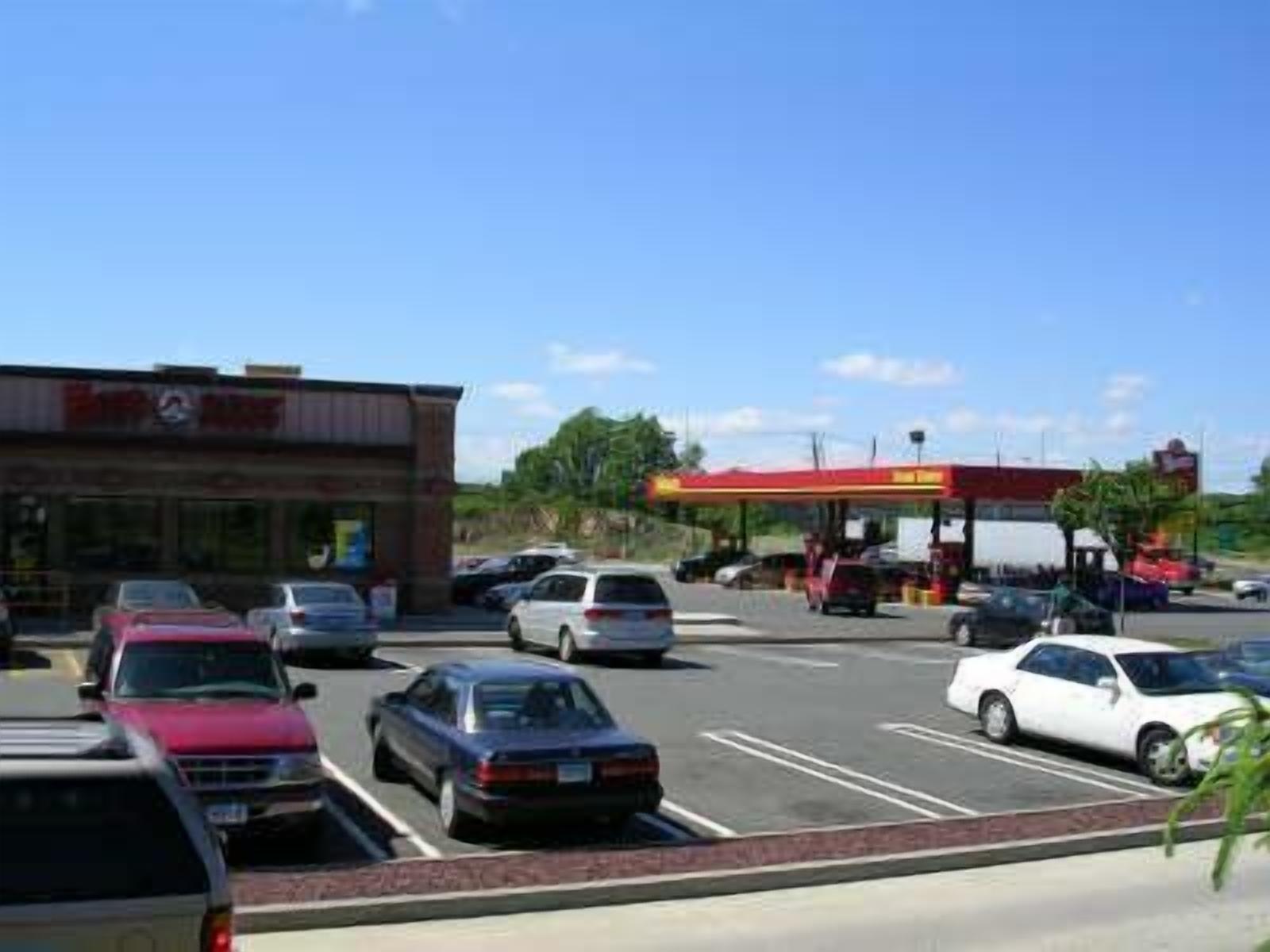 A parking lot with several cars, a gas station, and a building with a sign that reads "Easy Way."