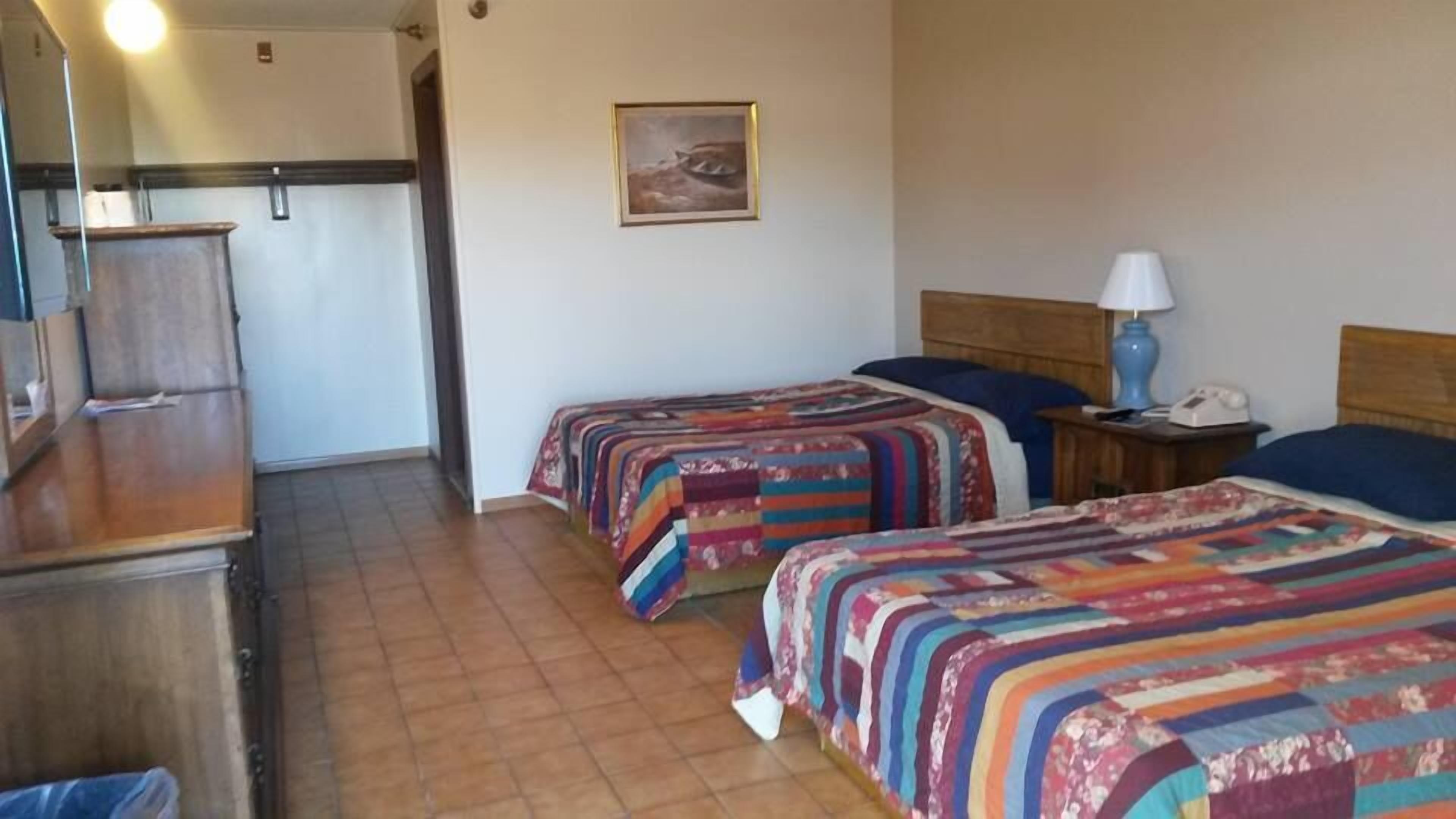 A hotel room with two beds, a wooden headboard, a nightstand with a lamp, and a painting on the wall.