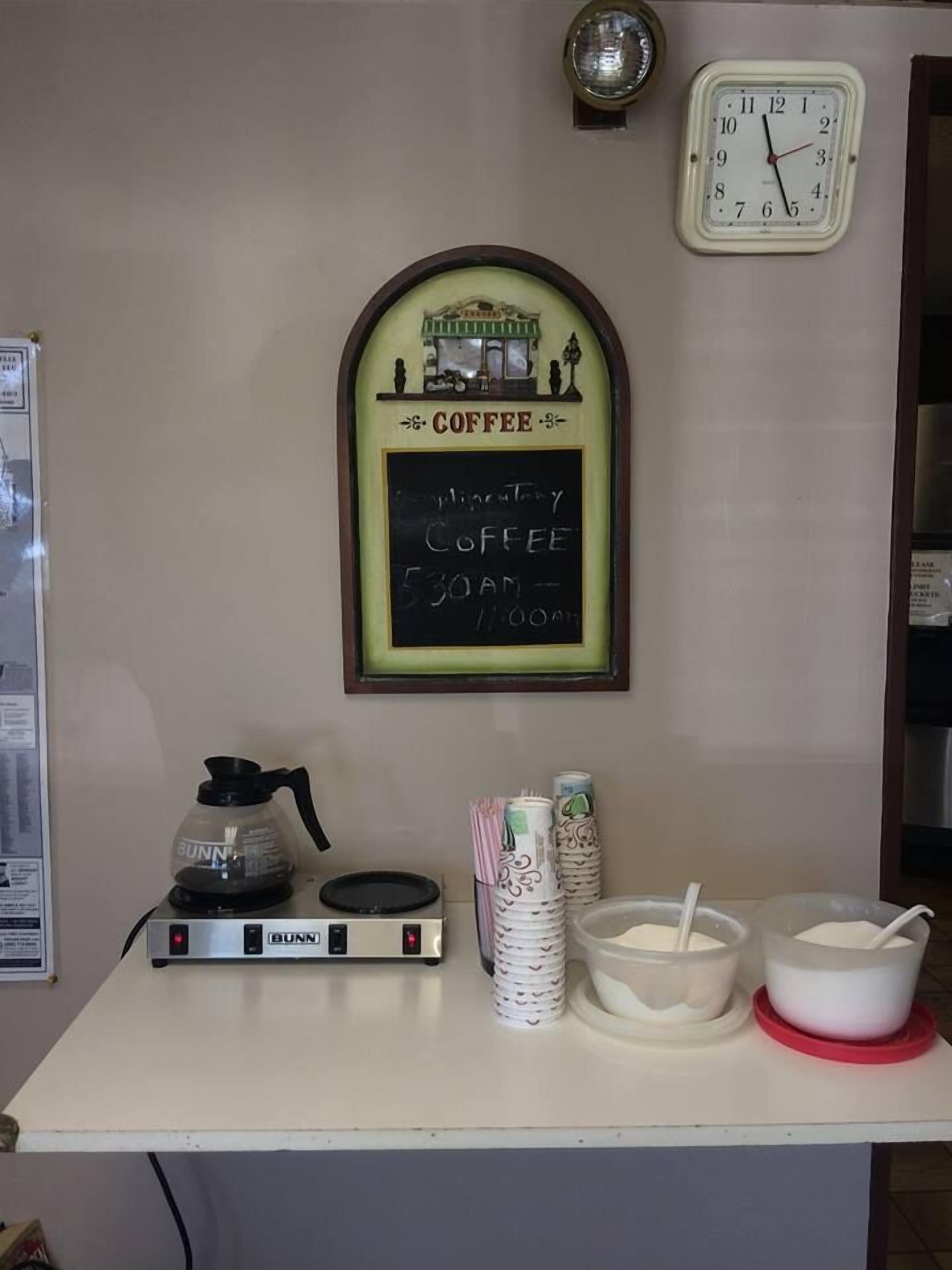 A coffee shop counter with a Bunn coffee maker, a chalkboard menu, and a clock on the wall.