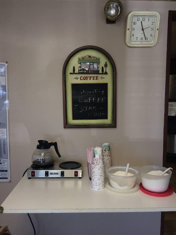 Una barra de cafetería con una máquina de café Bunn, un menú en una pizarra y un reloj en la pared.