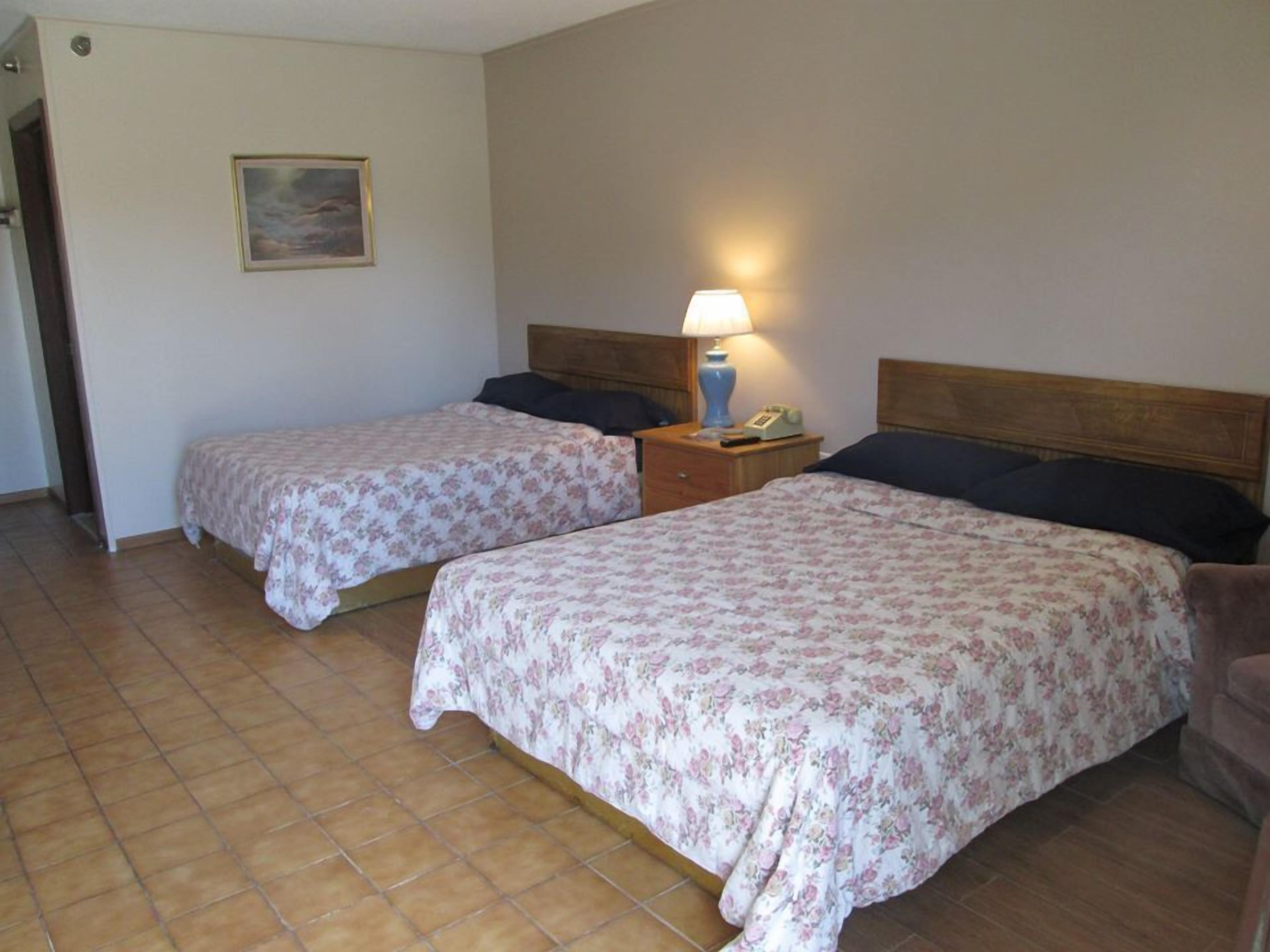 Une chambre avec deux lits, chacun agrémenté d’une literie à motifs floraux, une table de chevet avec une lampe et un tableau au mur.