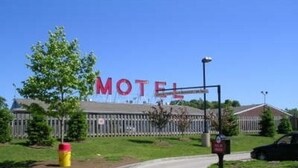 Ein Motel mit einer großen Schautafel, einem Parkplatz und einem Zaun im Hintergrund.