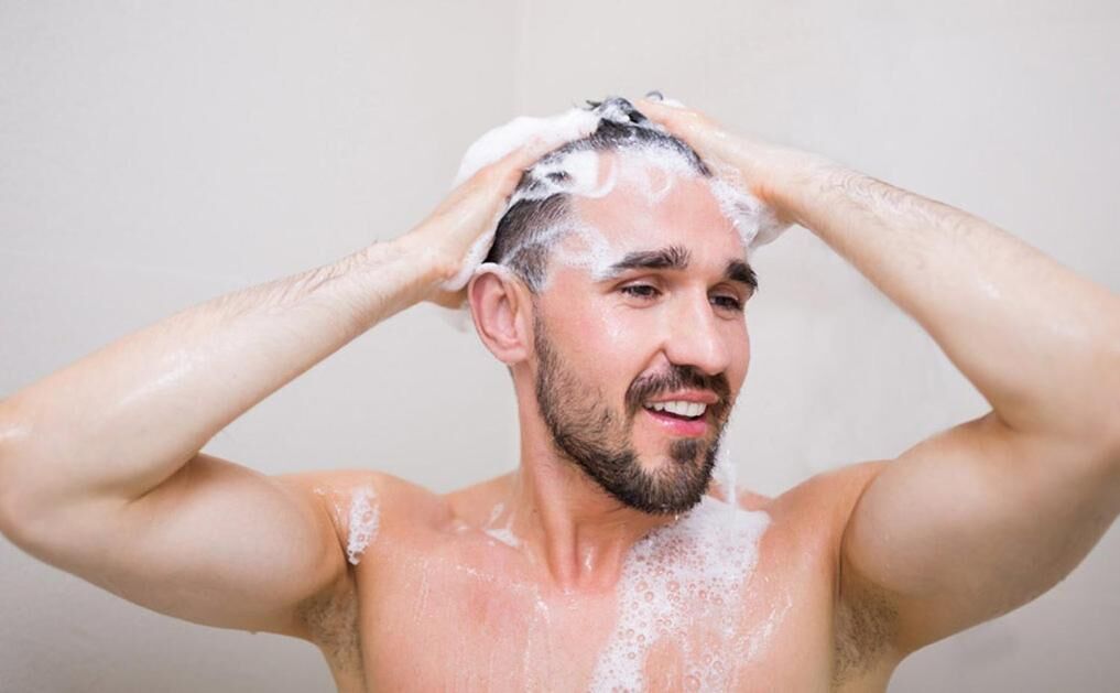 Una persona con espuma de jabón en la cabeza y los hombros, lo que sugiere una ducha o un baño.