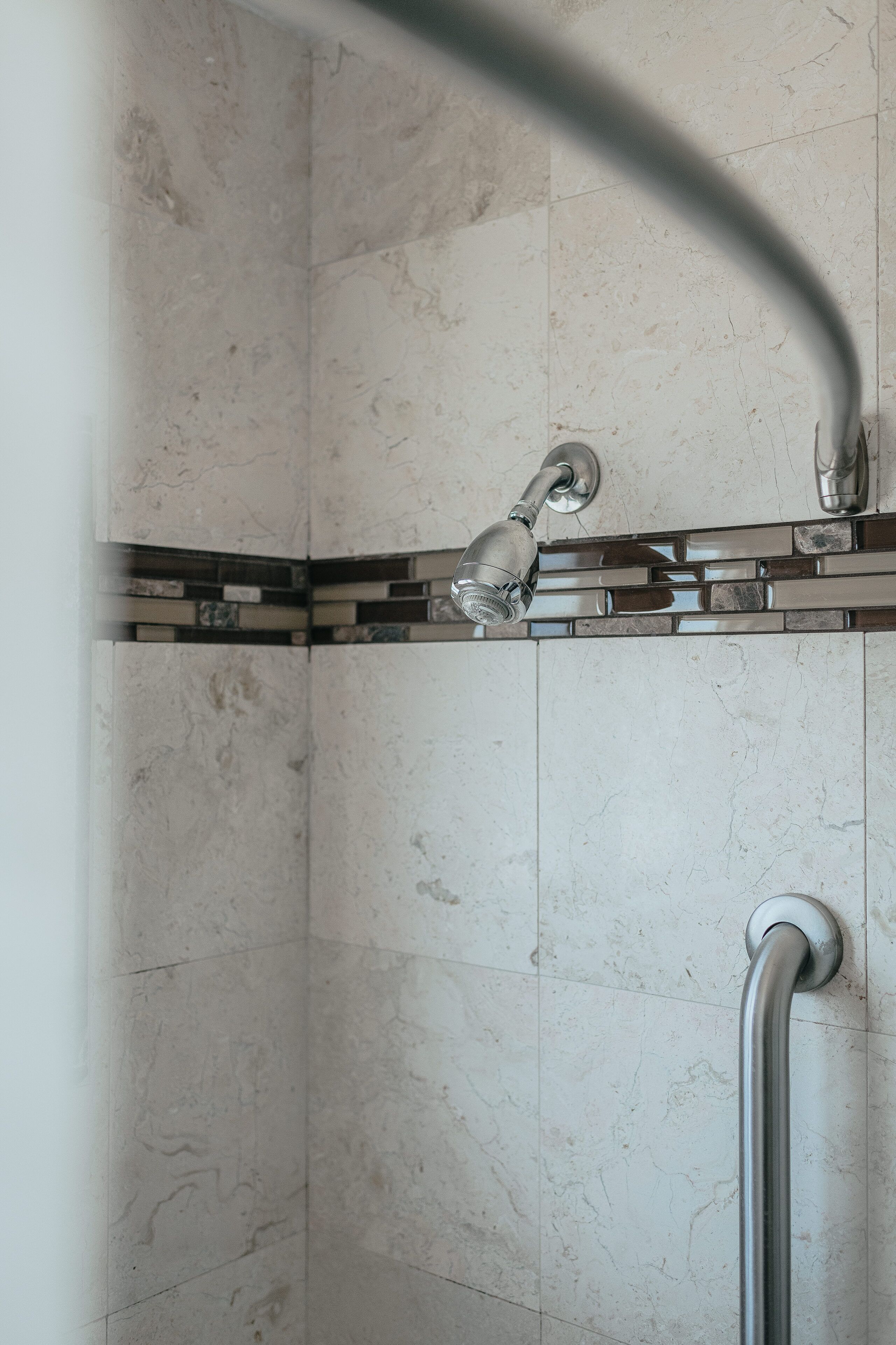 A shower area with a handheld showerhead, a glass-enclosed shower, and a handrail.