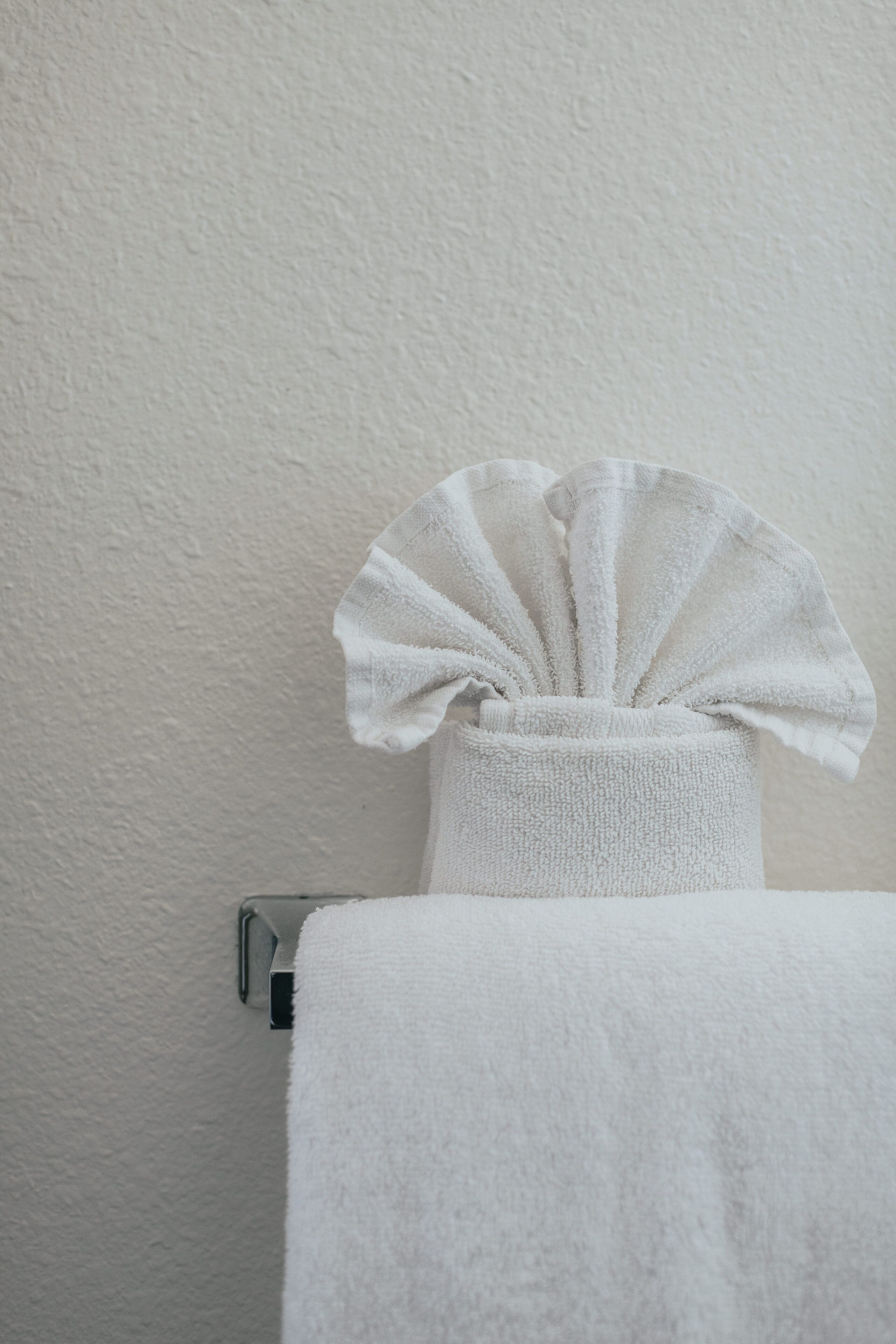 A white towel hanging on a metal towel rack against a textured wall.