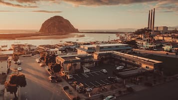 An aerial view of a coastal town with a prominent mountain, a marina with boats, and a large industrial building with tall chimneys.