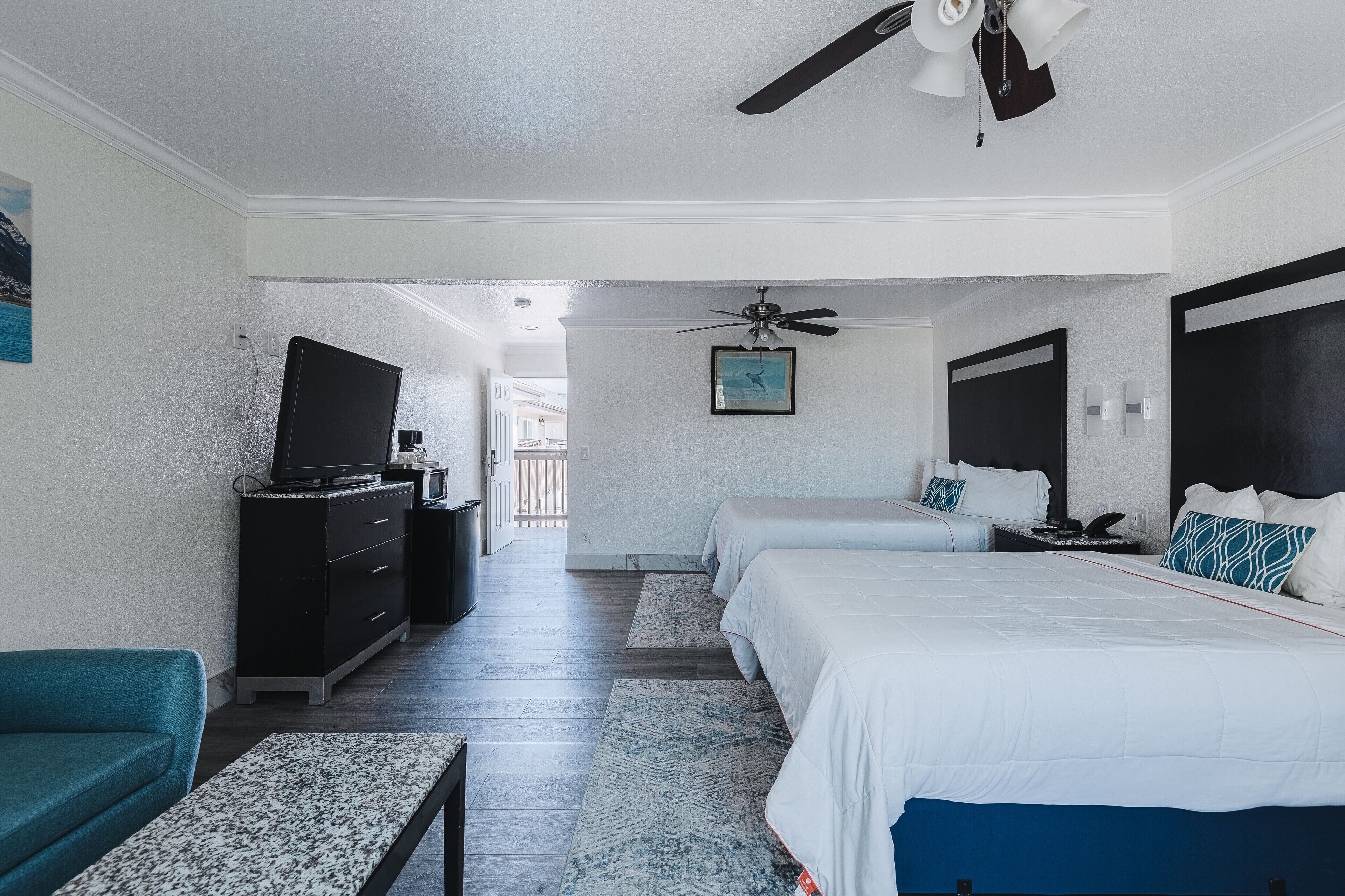 Quarto de hotel com duas camas, televisão, ventoinha no teto e vista para o corredor.