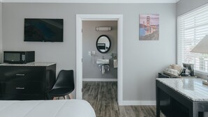 Hotelkamer met een bed, een bureau met een magnetron, een televisie, een badkamer met een wastafel en spiegel, en een raam met jaloezieën.