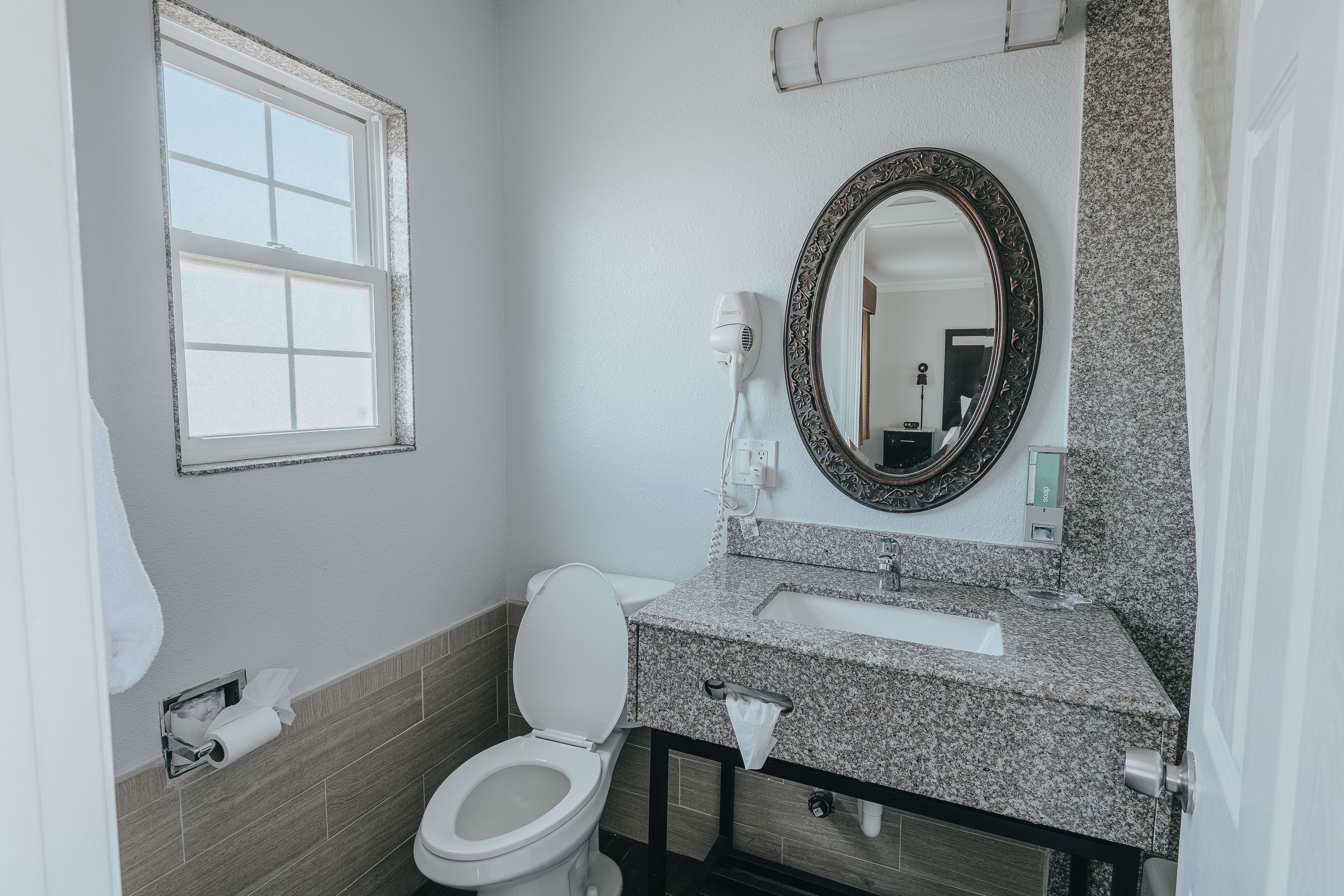A bathroom with a toilet, sink, mirror, and window.