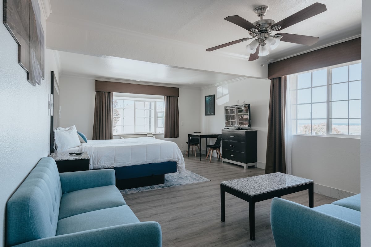 Habitación de hotel moderna con cama, escritorio, ventilador de techo y vistas al exterior.