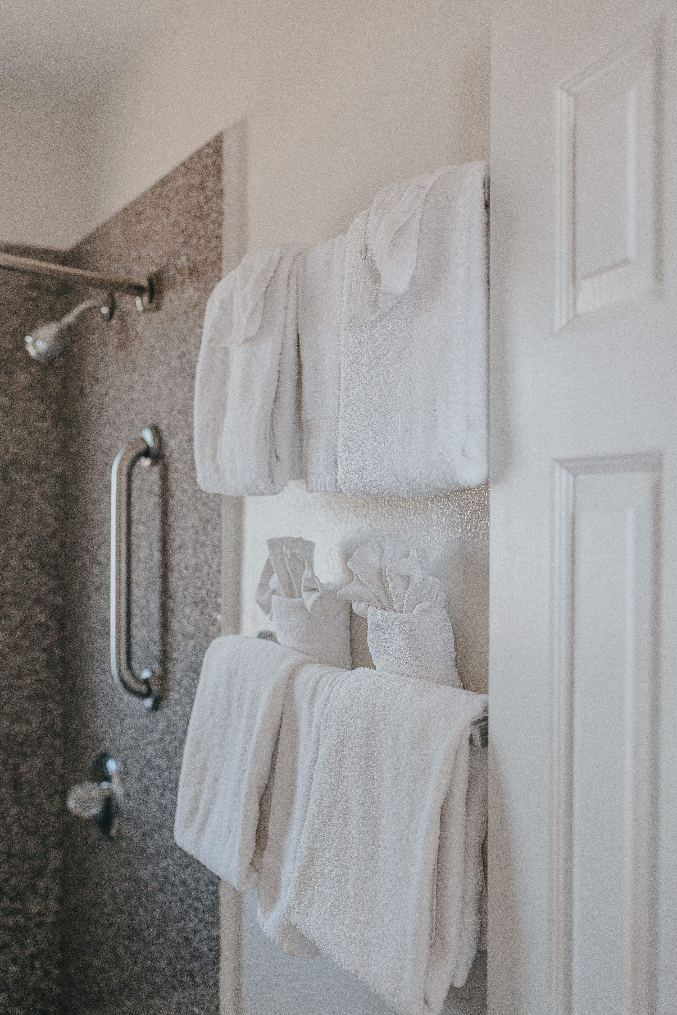 A bathroom with a shower, a towel rack with folded towels, and a handrail.