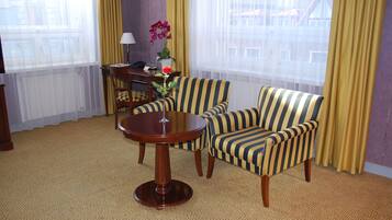 Habitación de hotel con sillones a rayas, una mesa redonda, un escritorio pequeño con lámpara y una orquídea en maceta.
