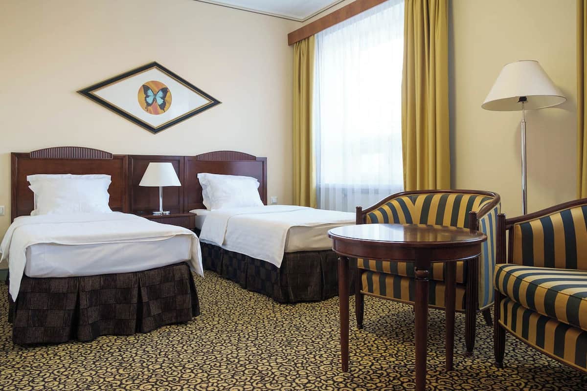 Ein Hotelzimmer mit zwei Betten, einem kleinen Tisch, einem Stuhl, einer Lampe und einem gerahmten Bild an der Wand.