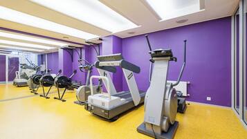 A gym with various cardio machines, a yellow floor, and purple walls.