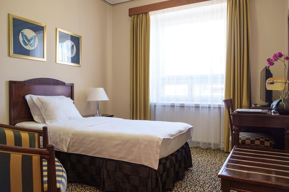 Ein Hotelzimmer mit einem Bett, einem Schreibtisch, einem Sessel, einer Lampe und zwei gerahmten Bildern an der Wand.