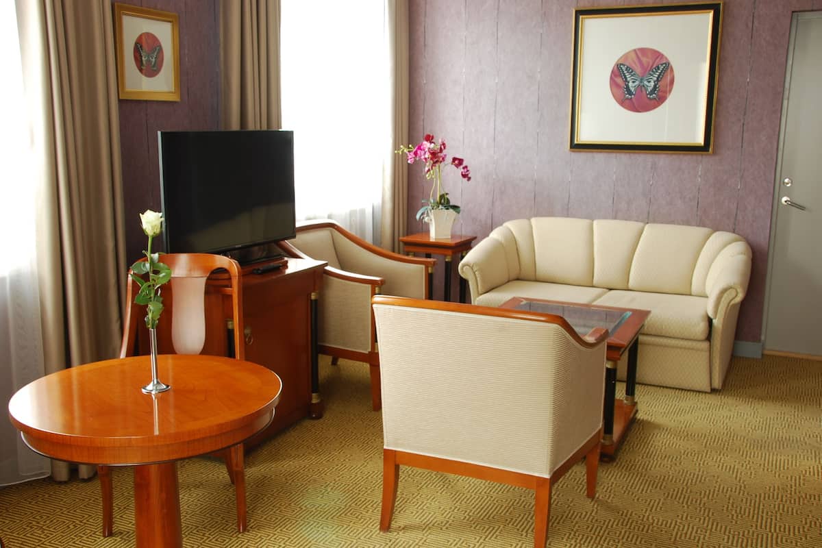 Ein Hotelzimmer mit Fernseher, einer Couch, einem Esstisch und einem Stuhl.
