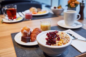A breakfast setting with a bowl of cereal, a croissant, and a glass of juice on a table.